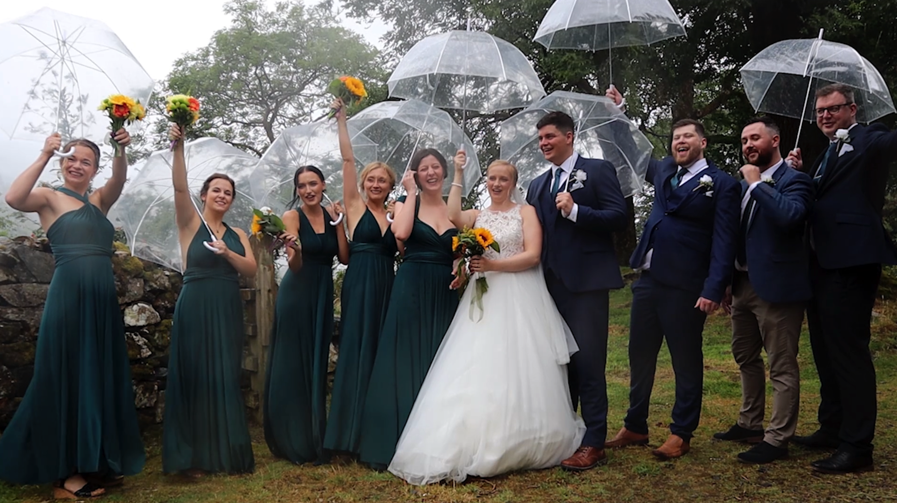 Husband, Bride, Groomsmen and Bridemades line up outside under umberellas