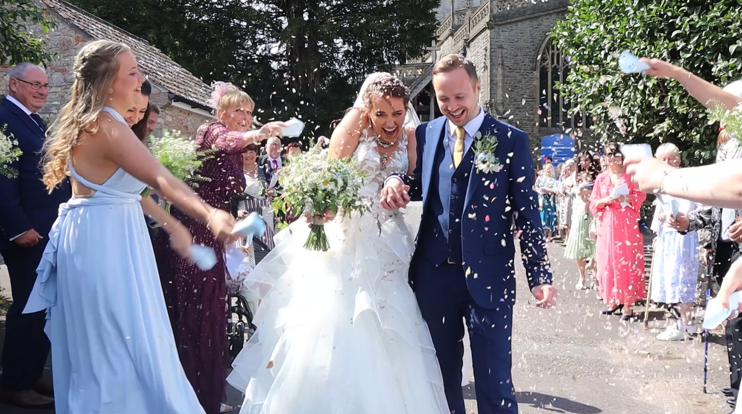 Wide picture of Husband and Bride walking away from wedding venue laughing having confetti thrown on them