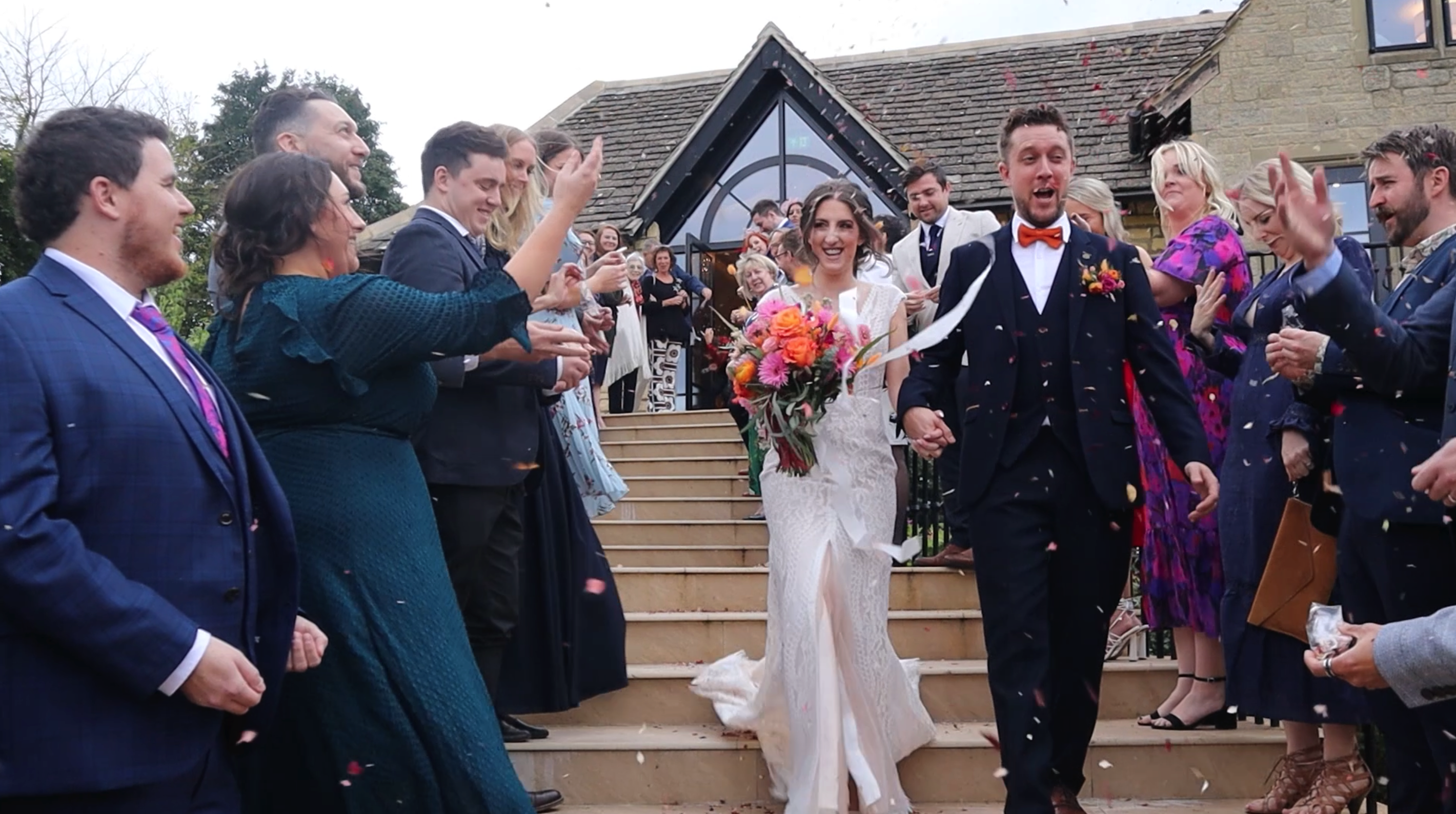 Husband and Bride walking down stairs from wedding venue laughing having confetti thrown on them