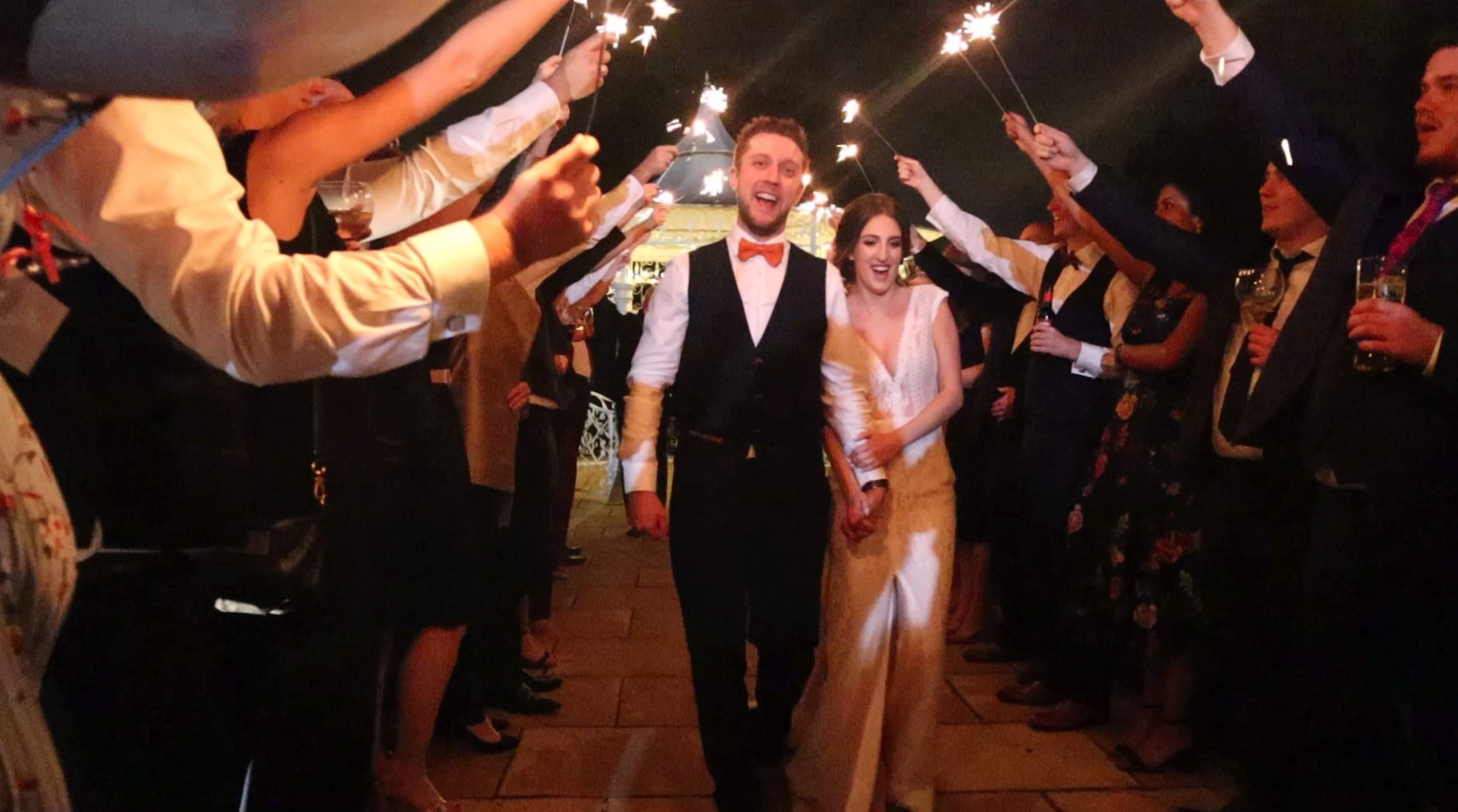 Husband and Bride walking through line of people at night under a bridge of sparklers